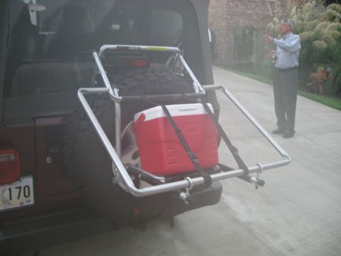 1995 Ford Bronco - Rear view of a Jeep Wrangler equipped with a spare tire carrier and a red cooler, with a man standing nearby.