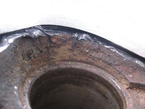 1979 Ford F-150 - Extreme close-up looking down into a rusty machined bore in a cast iron part, with a bead of black RTV sealant smeared along the sealing ed…