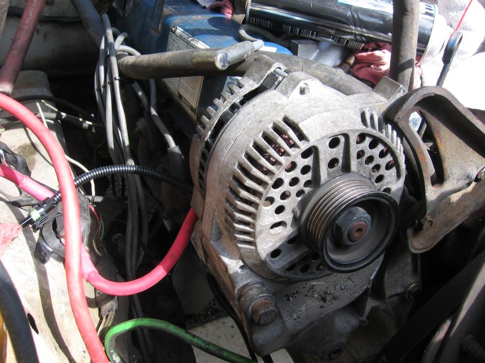 Alternator with red and green wires in a cluttered engine bay. Text 'SUPERMOTORS' visible