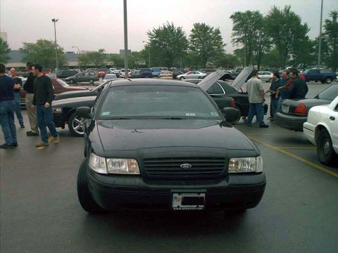 2000 Ford Crown Victoria - Front view of a black 2000 Ford Crown Victoria in a parking lot with several other vehicles and individuals present.