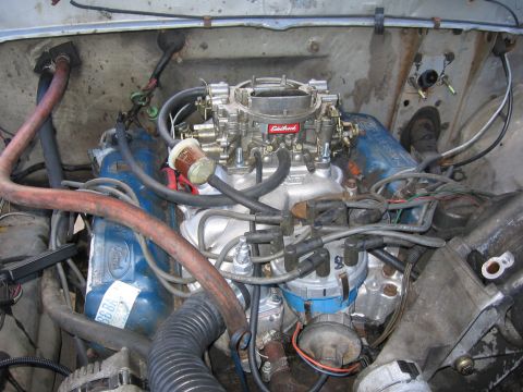1979 Ford F-150 - Overhead view into the engine bay of a stripped truck, showing a Ford V8 with blue valve covers, a polished aluminum intake manifold topped…