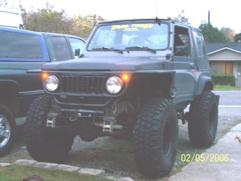 1988 Suzuki Samurai - Modified 1988 Suzuki Samurai sits parked next to another vehicle, showing off its off-road tires.