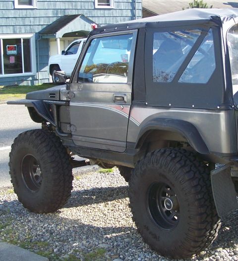 1988 Suzuki Samurai - A modified Suzuki Samurai is shown from the front-three-quarter view, with a white pickup truck in the background.