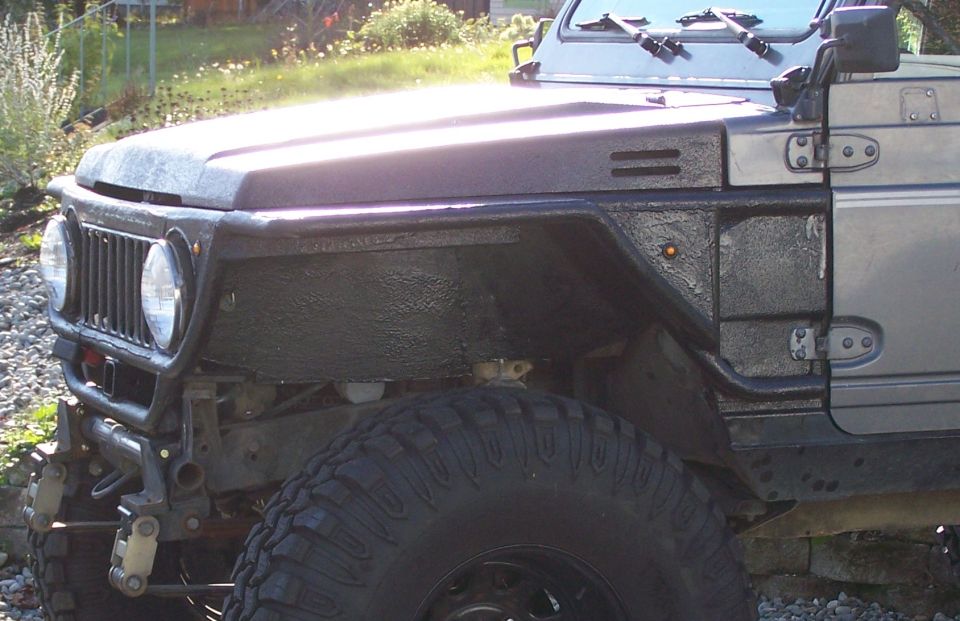 Grey bedliner-coated trail rig front corner with tube bumper and cut fenders