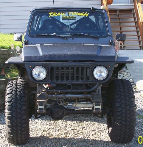 1988 Suzuki Samurai - This modified off-road SUV features oversized tires and a "TRAV TOUGH" sticker on the windshield.