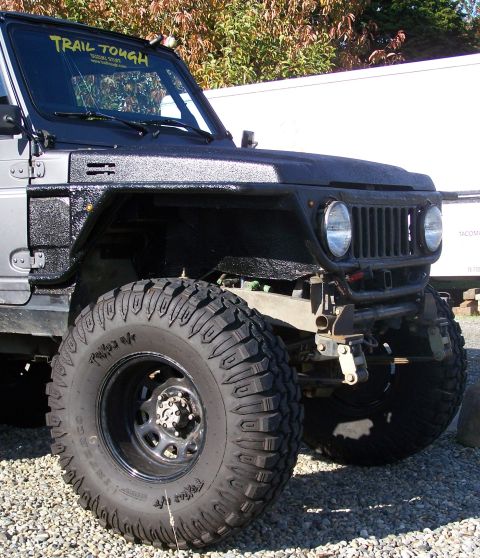 1988 Suzuki Samurai - A modified Suzuki Samurai with aggressive tires and a "Trail Tough" decal is shown from a low front three-quarter angle.