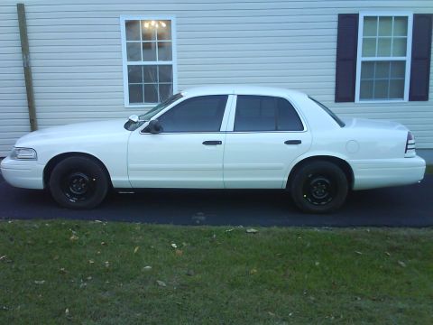 2003 Ford Crown Victoria - A white 2003 Ford Crown Victoria sedan is parked on asphalt in front of a house.