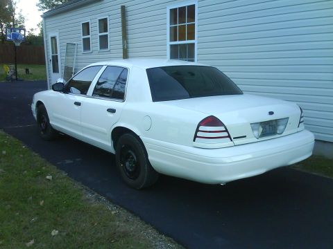 2003 Ford Crown Victoria - This white 2003 Ford Crown Victoria is seen from the rear quarter angle, black steel wheels and parked next to a residential building.