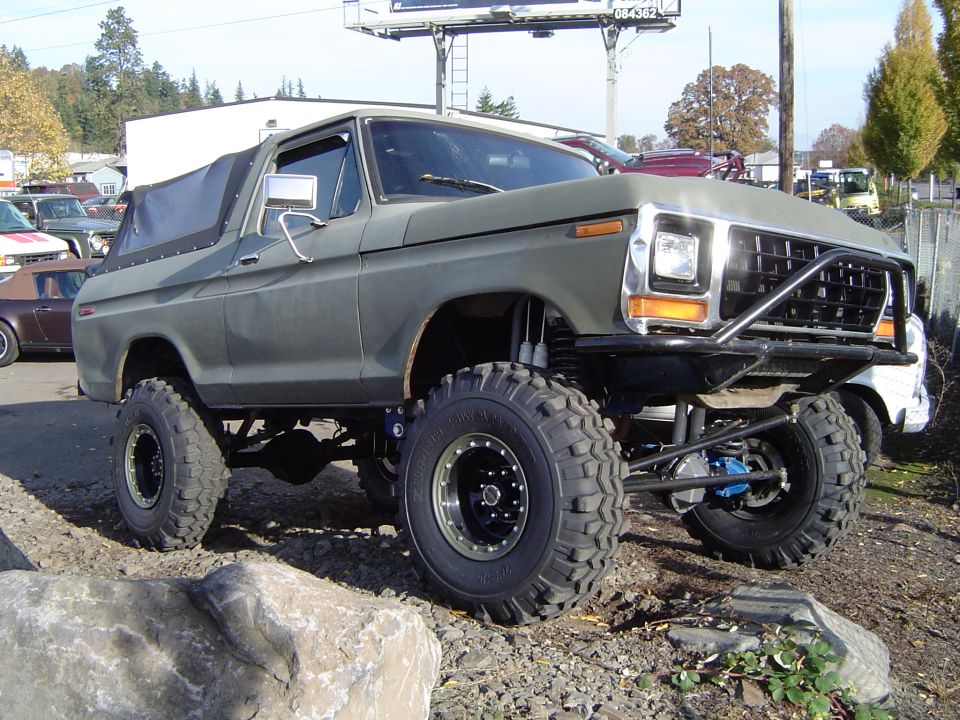Lifted olive-drab late-1970s Ford Bronco on large off-road tires at a lot