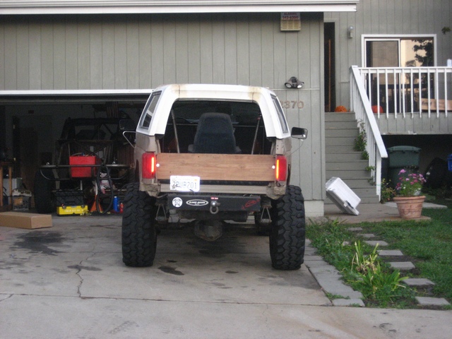 Rear of white lifted Bronco with wood dovetail bed panel and big tires on driveway