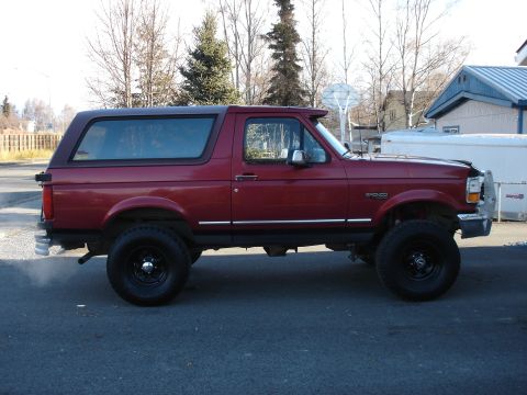 1996 Ford Bronco - Side profile of a red 1996 Ford Bronco with aftermarket wheels and tires.