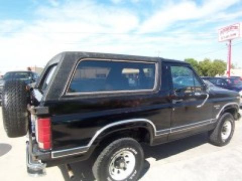 1986 Ford Bronco - This black SUV has a spare tire mounted on the rear door and is seen from a rear quarter angle.