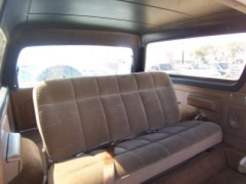 1986 Ford Bronco - The interior of a 1986 Ford Bronco is visible, a tan bench seat and large windows.