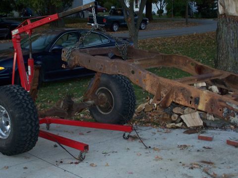 1979 Ford F-150 - A heavily rusted truck frame is being lifted by an engine hoist in a driveway.