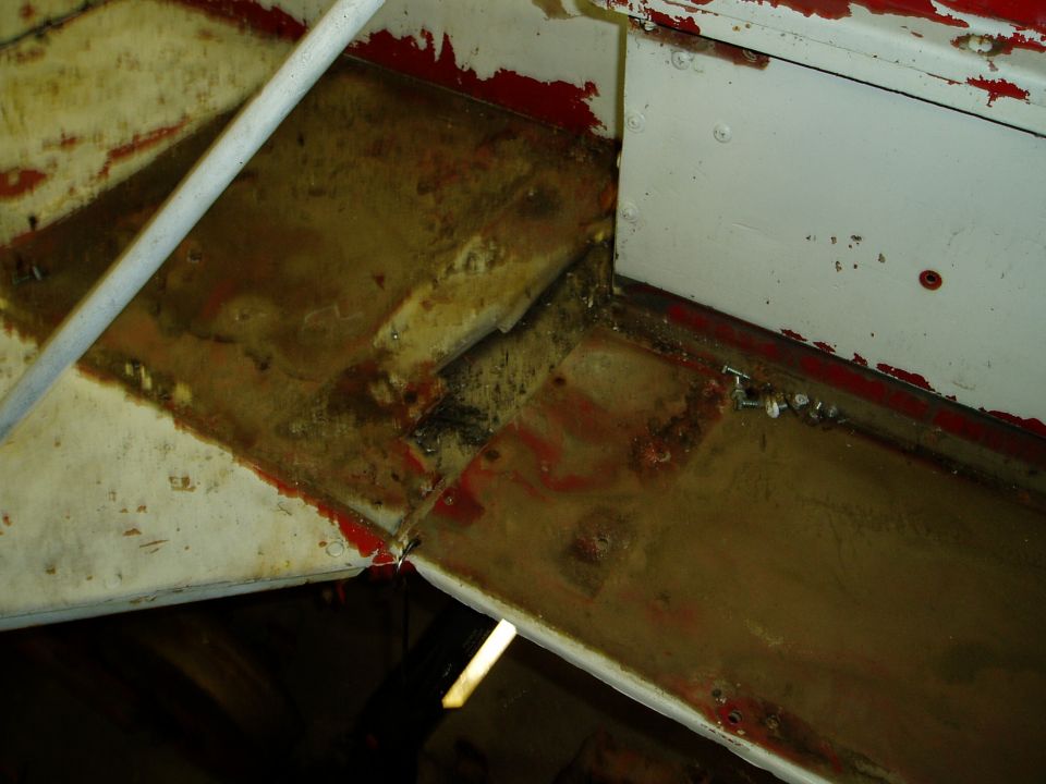 Close-up of dirty, rusty metal frame and white paneling on vehicle undercarriage