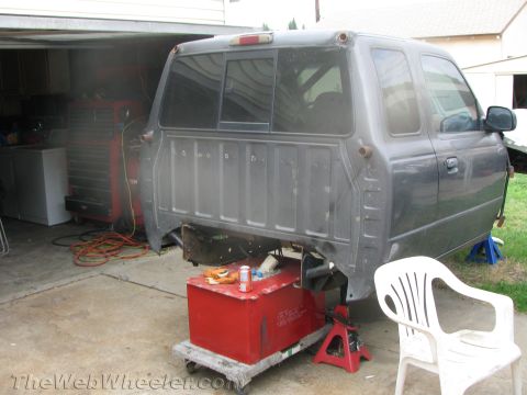 1968 Ford Mustang - A gray pickup truck bed and cab are supported by jack stands in a garage, with a red fuel tank positioned below.