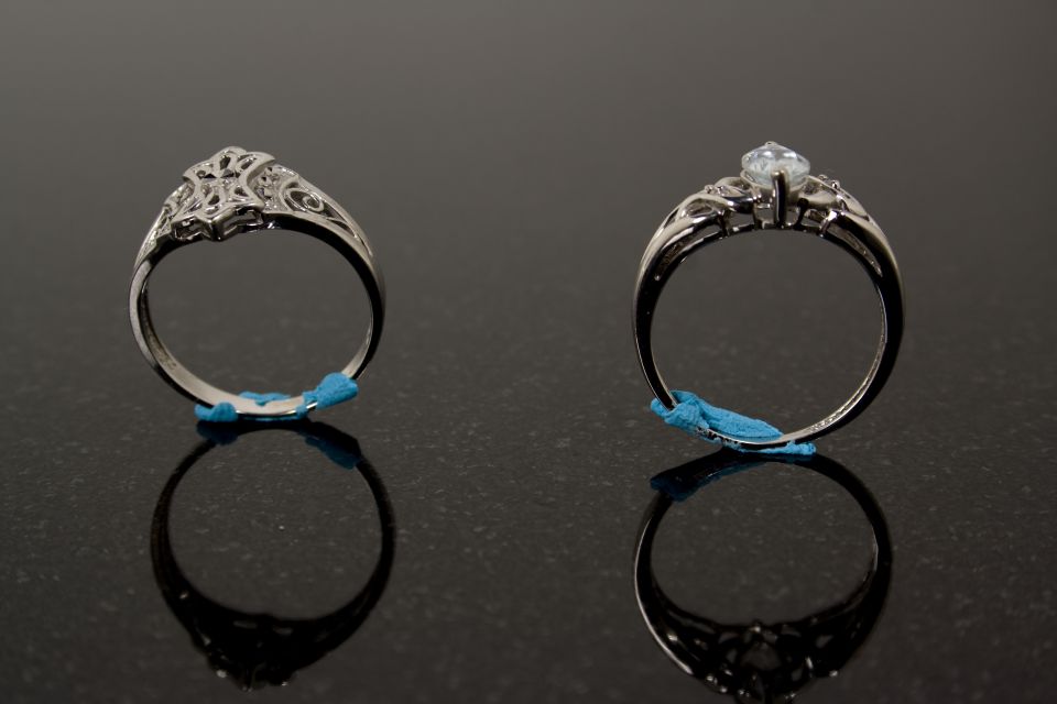 Two silver filigree rings, one with a clear gemstone, on a reflective surface
