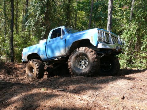 1988 Ford Bronco - This lifted blue pickup truck navigates a muddy trail with its large off-road tires.