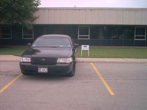 2000 Ford Crown Victoria - A black Ford Crown Victoria is parked in front of a building with large windows.