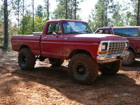 1988 Ford Bronco - A red pickup truck with oversized tires is shown off-road, with another vehicle partially visible in the background.