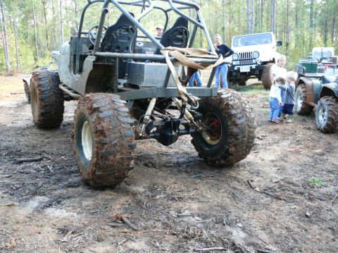 1988 Ford Bronco - A group of vehicles, including a heavily modified buggy, a Jeep, and an ATV, are gathered in a muddy, wooded area.