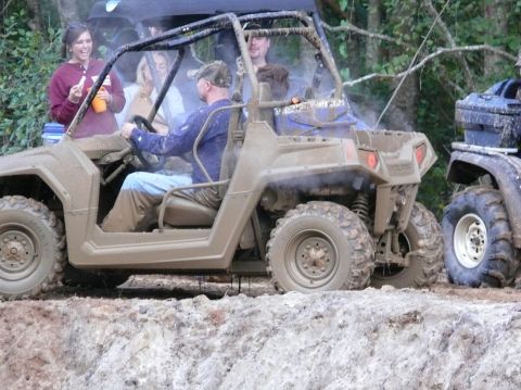 1988 Ford Bronco - An off-road vehicle covered in mud navigates a rough terrain with passengers.