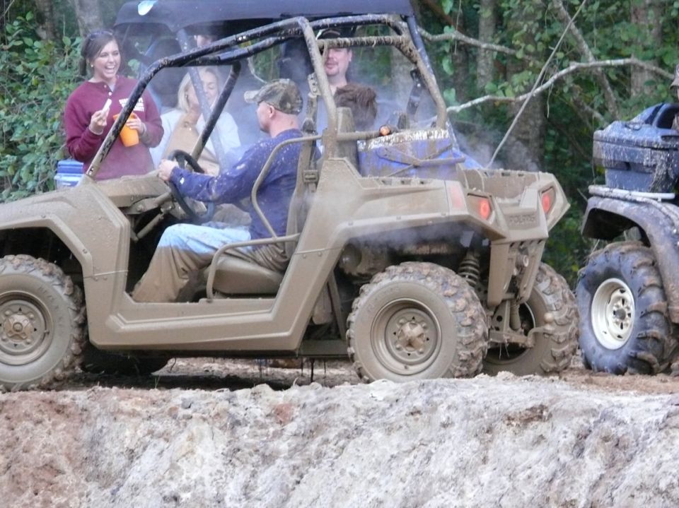 Mud-covered off-road vehicle with people inside, driving on a dirt track