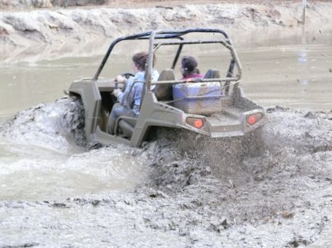 1988 Ford Bronco - A side-by-side UTV navigates through a muddy terrain, kicking up water and mud.