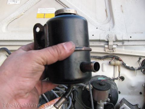 1987 Suzuki Samurai - A hand holds a black power steering fluid reservoir, with engine components visible in the background.
