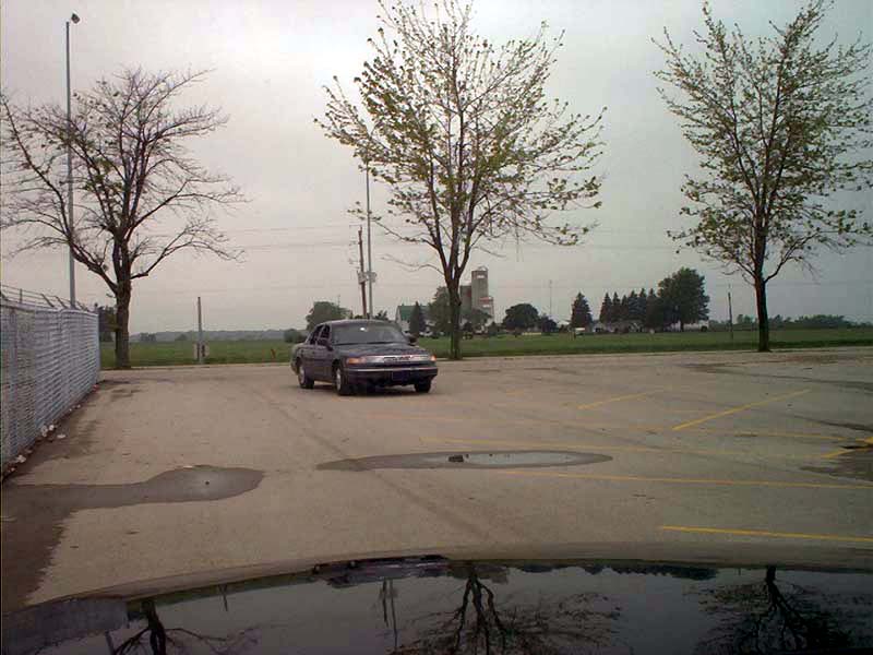 Dark sedan parked in a lot, trees and buildings in background