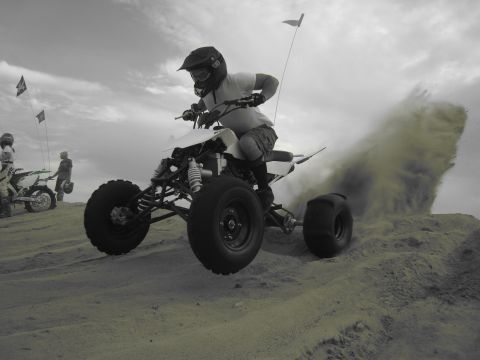 1996 Ford Bronco - An ATV rider takes flight over a sand dune, creating a large plume of dust behind them.