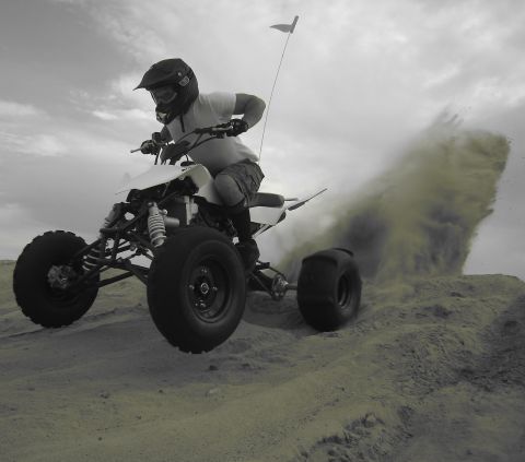 1996 Ford Bronco - A person rides a quad bike through a dusty sand dune, with a flag on a pole attached to the vehicle.