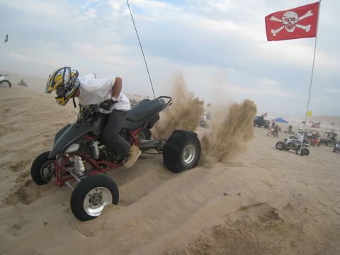 1996 Ford Bronco - An ATV powers through the sand at Dumont Dunes, with a pirate flag visible in the background.