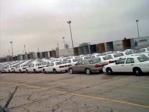 2000 Ford Crown Victoria - A large group of white Ford Crown Victoria sedans are parked in an outdoor lot under a cloudy sky.