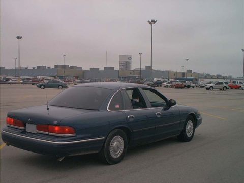 2000 Ford Crown Victoria - Dark blue 2000 Ford Crown Victoria parked in a lot with other vehicles and a large building in the background.