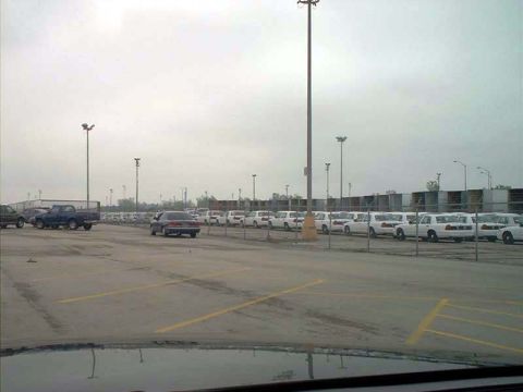 2000 Ford Crown Victoria - A large parking lot is filled with vehicles, including a row of white cars and a blue pickup truck.