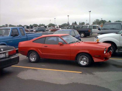 2000 Ford Crown Victoria - A red 1975 Ford Mustang II coupe is parked in a lot with other vehicles.