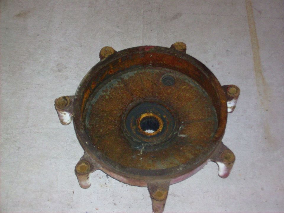 rusted metal part with six bolt holes, center bearing visible