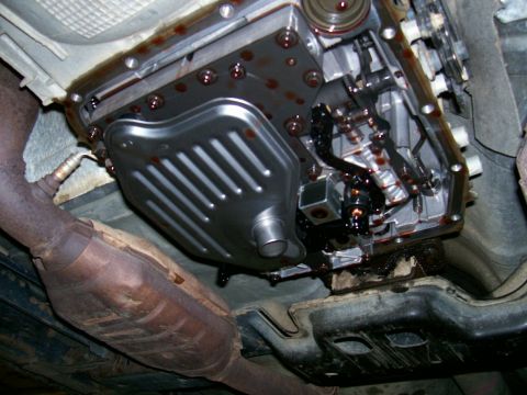 2001 Ford Crown Victoria - The underside of a vehicle displays a transmission pan with visible fluid leaks and a catalytic converter.