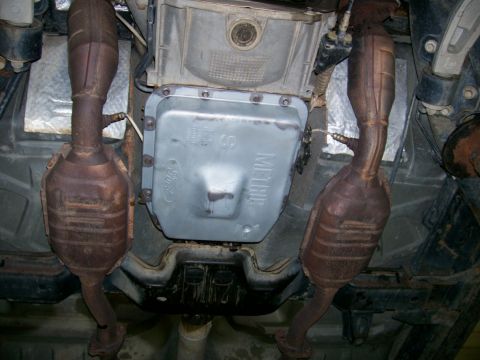 2001 Ford Crown Victoria - The transmission pan, bearing a Ford logo, is visible along with the catalytic converters and exhaust system.