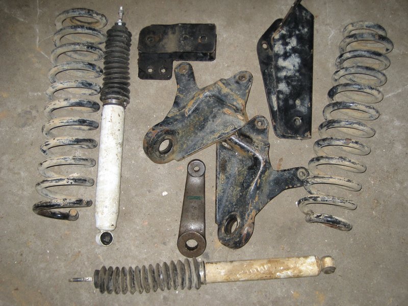 Used coil springs, white shocks, black brackets and a steering link laid out on a concrete floor