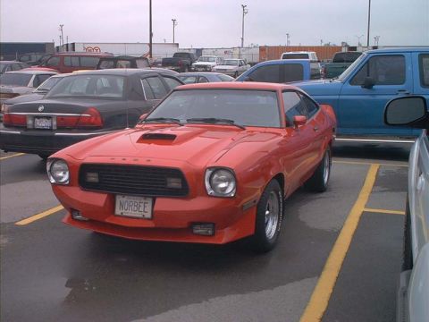 2000 Ford Crown Victoria - A red 1975 Ford Mustang II coupe is parked next to a black sedan and a blue truck.