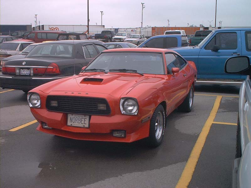 Red 1975 Ford Mustang II coupe with a hood scoop and a NORBEE license plate