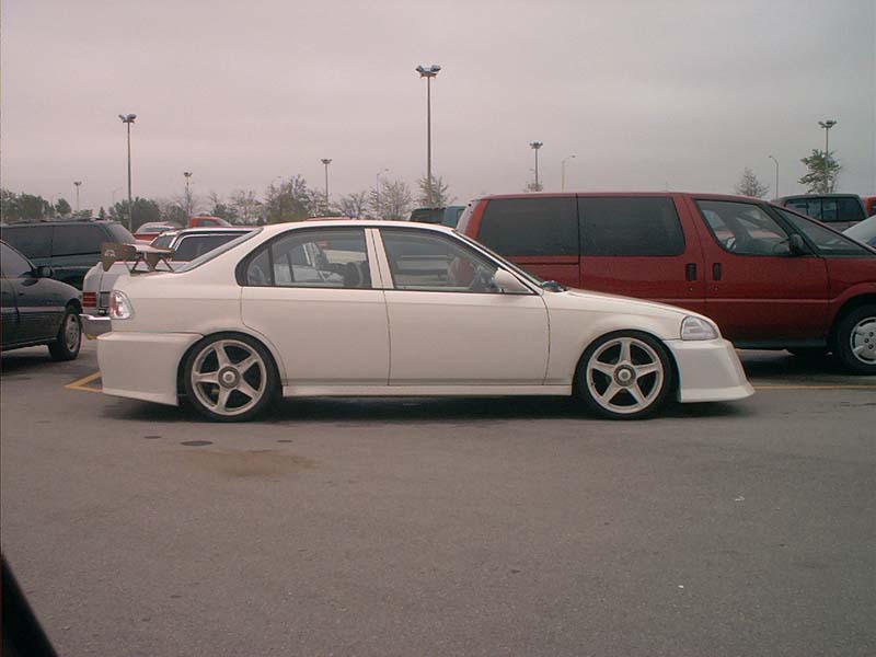 White sedan with a body kit and spoiler parked in a lot next to a red van