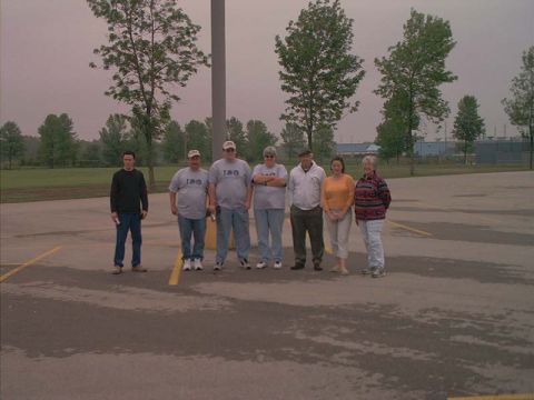 2000 Ford Crown Victoria - Seven people stand in a paved outdoor area with trees and a building in the background.