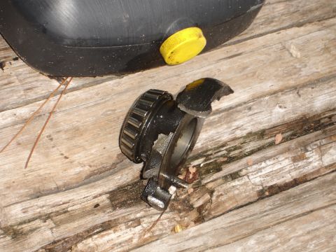 1989 Ford Bronco - A damaged wheel bearing assembly sits on a weathered wooden surface next to a black oil drain pan with a yellow cap.