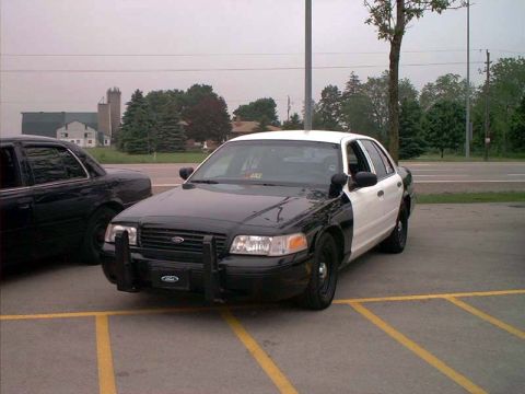 2000 Ford Crown Victoria - Two cars parked in a lot, one is a black and white police car.