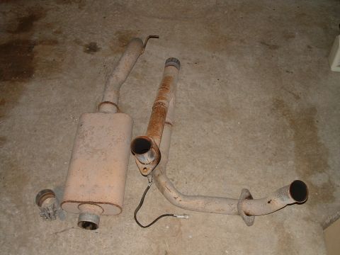1995 Ford Bronco - Two sections of an exhaust system, including a muffler and pipes, lie on a concrete surface.