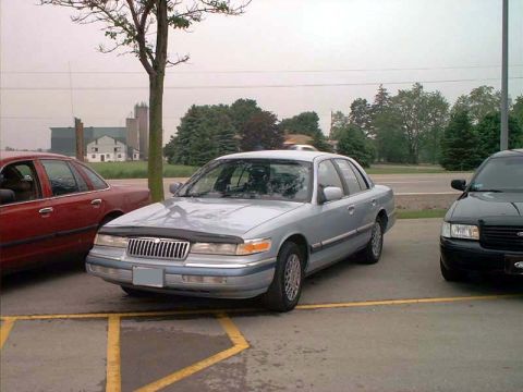 2000 Ford Crown Victoria - A silver sedan is parked next to a black vehicle in a parking lot.