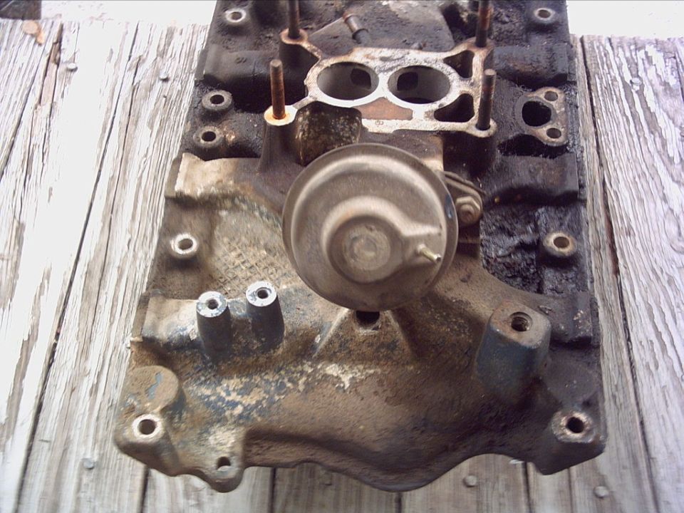 Dirty intake manifold with a vacuum actuator attached, resting on weathered wood